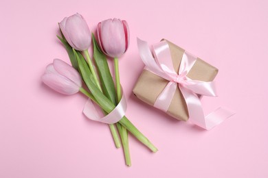 Beautiful gift box with bow and tulips on pink background, flat lay