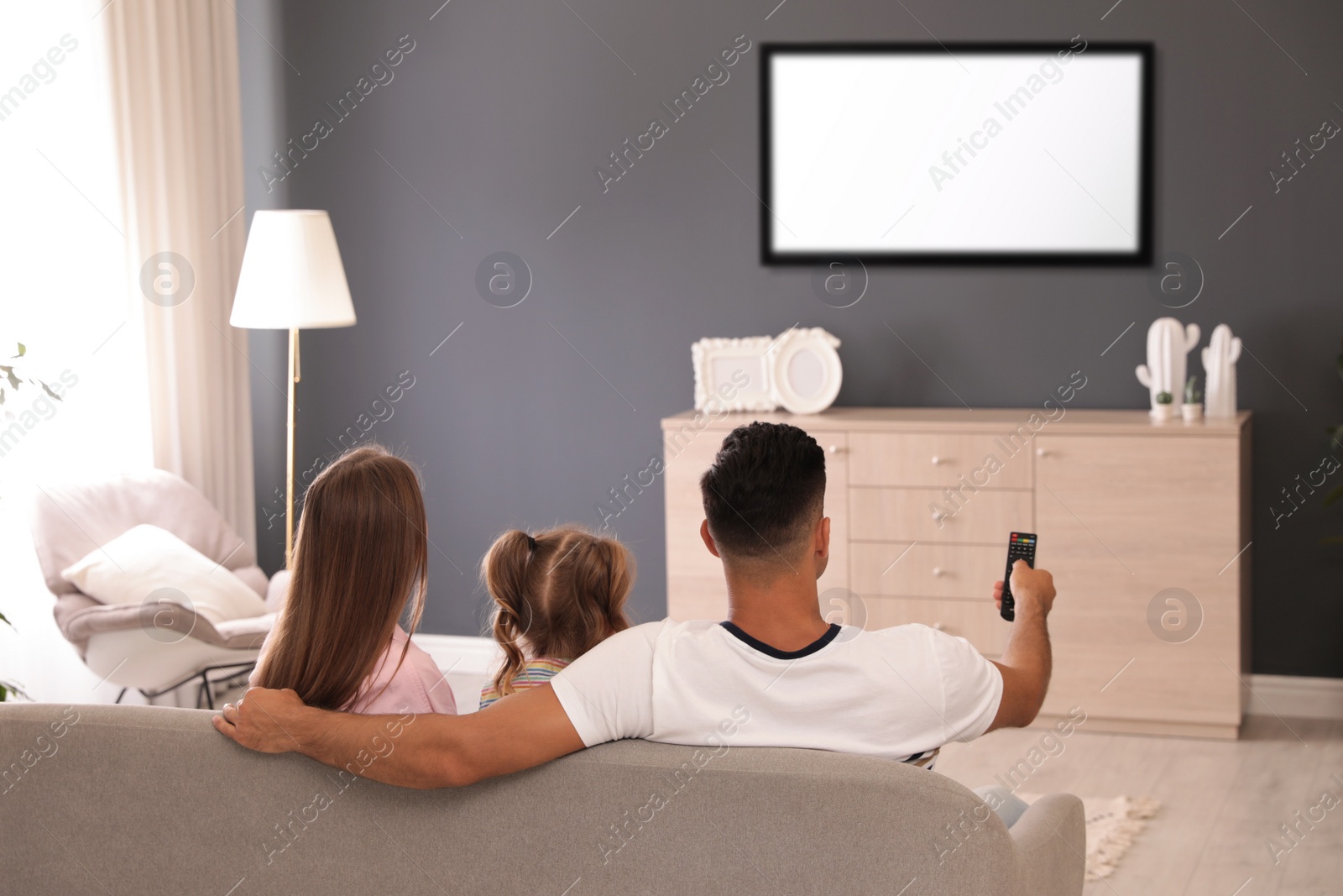 Photo of Family watching TV on sofa at home, back view