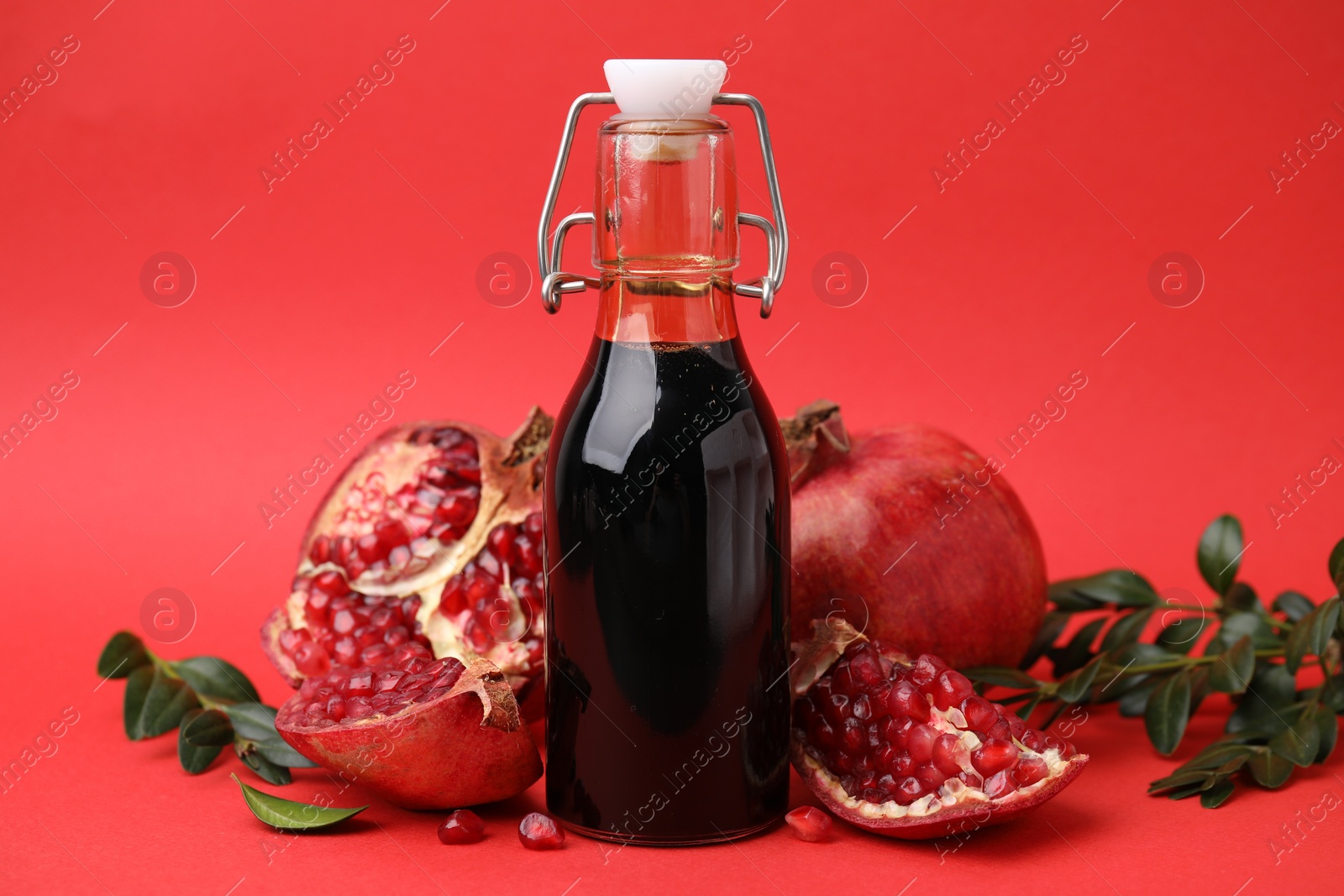 Photo of Tasty pomegranate sauce in bottle, branches and fruits on red background, closeup