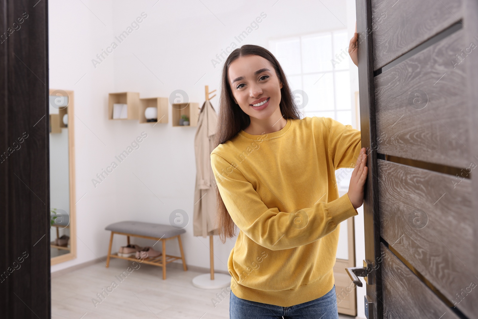 Photo of Happy woman standing near door, space for text. Invitation to come indoors