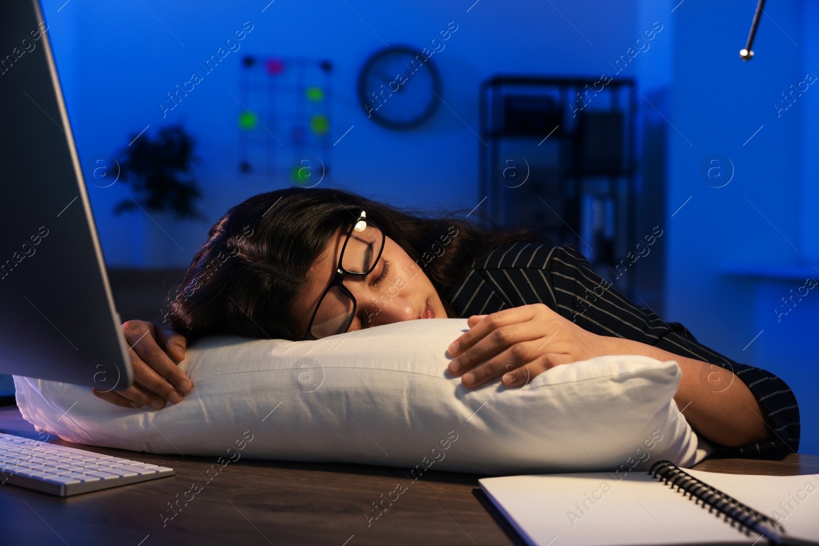 Photo of Tired overworked businesswoman napping with pillow at night in office