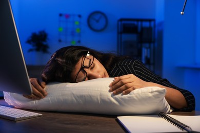 Photo of Tired overworked businesswoman napping with pillow at night in office