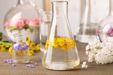 Photo of Laboratory glassware with flowers on wooden table. Extracting essential oil for perfumery and cosmetics