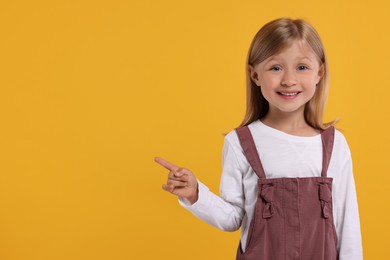 Photo of Special promotion. Little girl pointing at something on orange background. Space for text