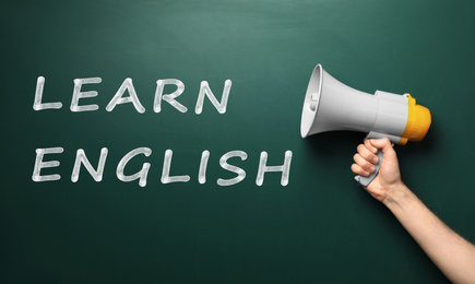 Man holding megaphone near green chalkboard with text Learn English, closeup