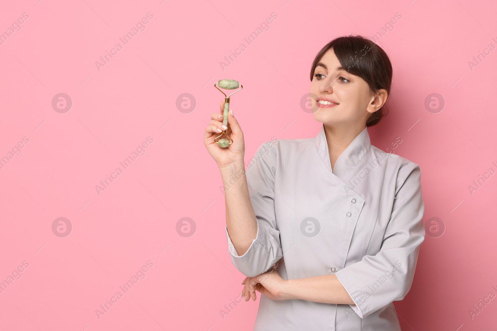 Photo of Cosmetologist with facial roller on pink background, space for text