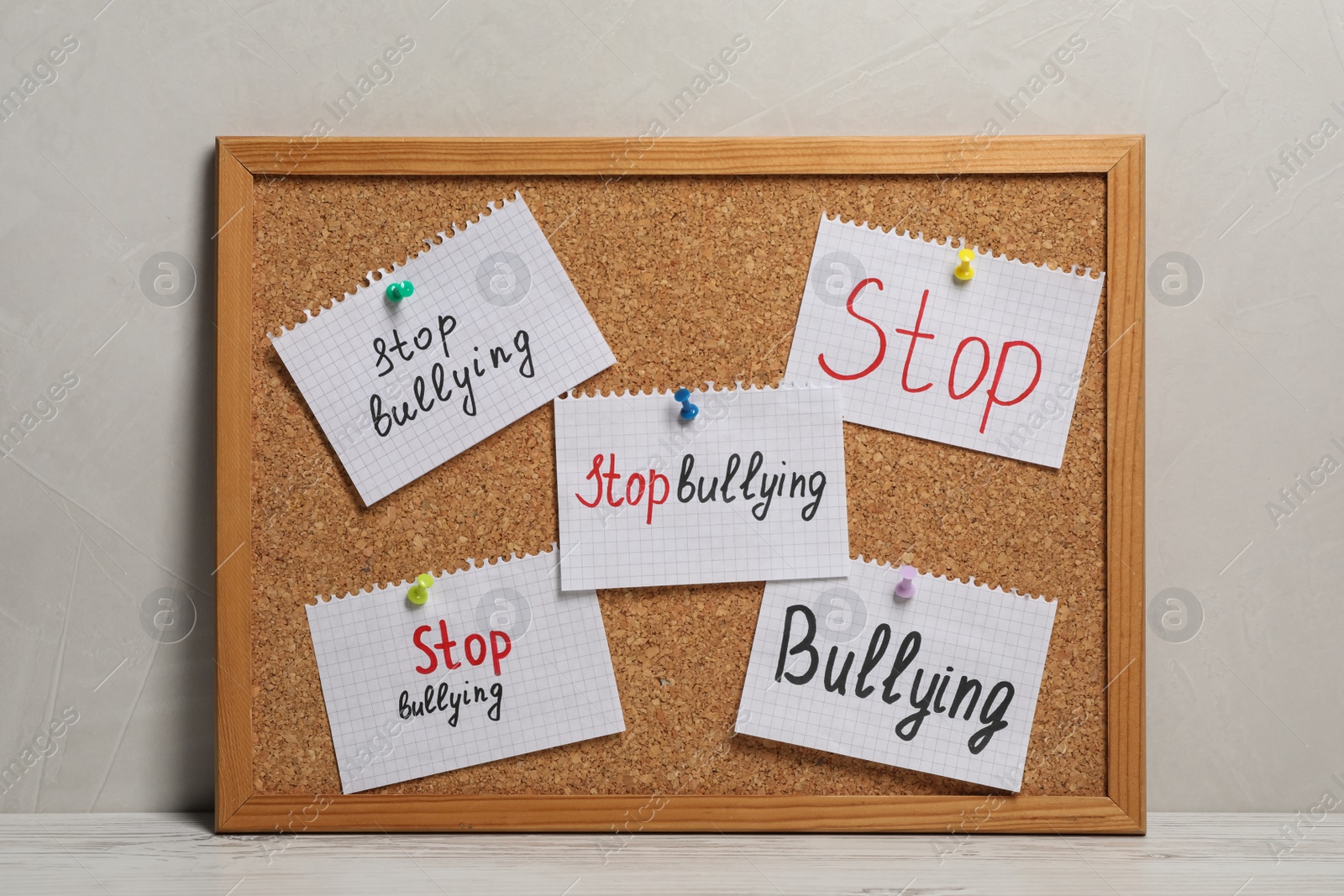 Photo of Notes with phrase Stop Bullying pinned to cork board on table near grey wall