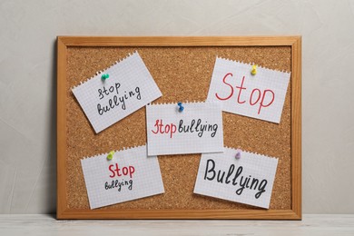 Photo of Notes with phrase Stop Bullying pinned to cork board on table near grey wall
