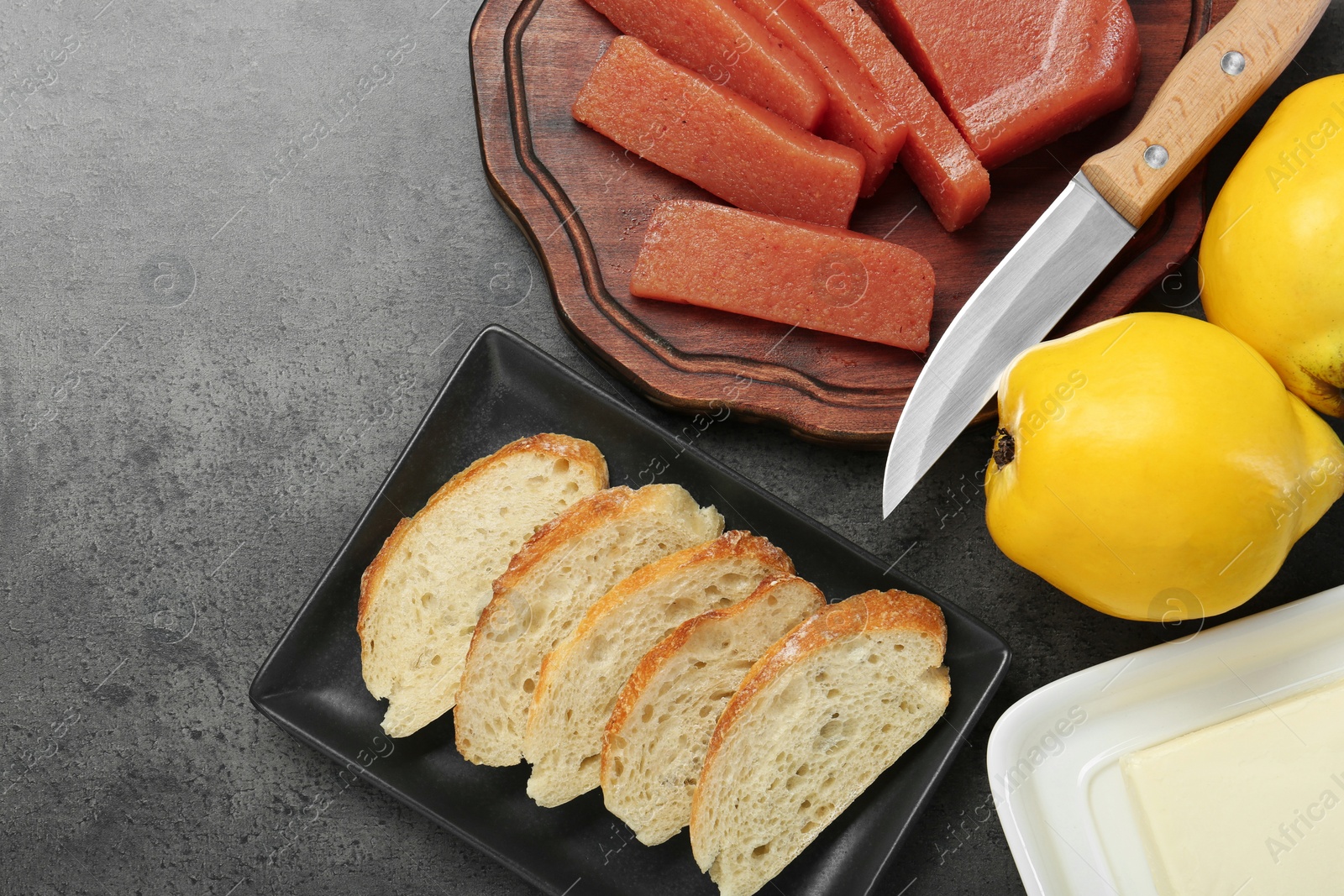 Photo of Delicious quince paste, bread, butter and fresh fruits on grey textured table, flat lay. Space for text