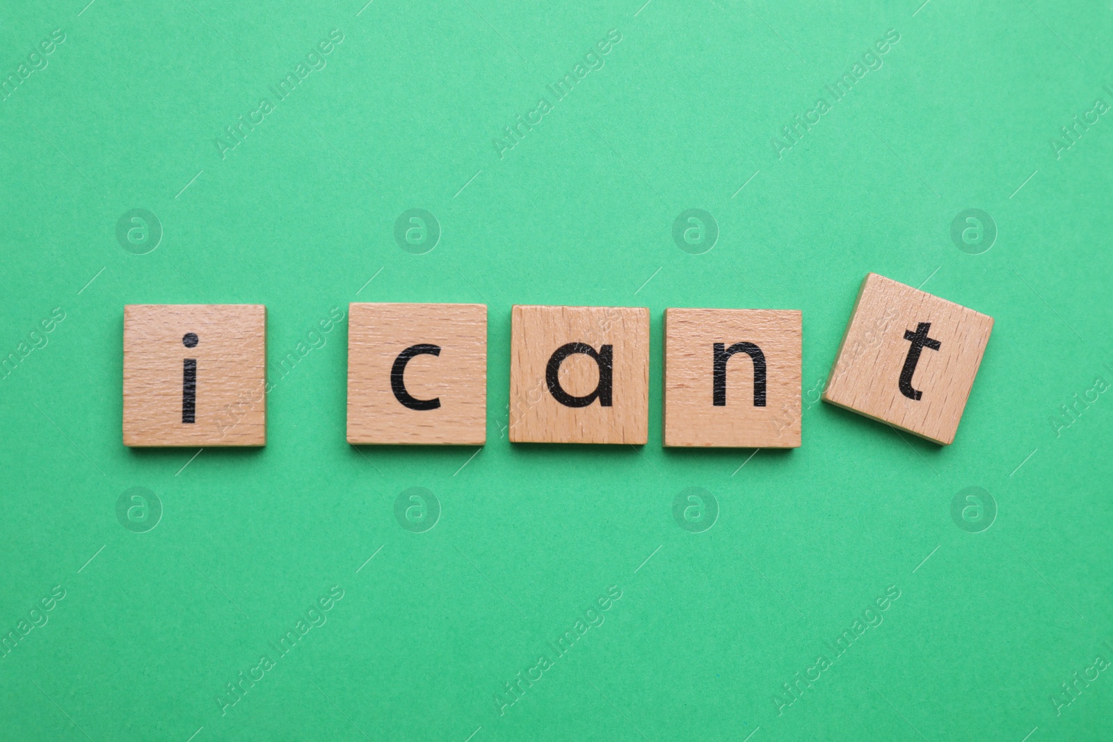 Photo of Motivation concept. Changing phrase from I Can't into I Can by removing wooden square with letter T on green background, top view