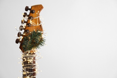Photo of Guitar with fairy lights and fir branch on white background. Christmas music