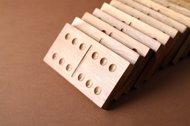 Photo of Fallen wooden domino tiles on brown background, closeup