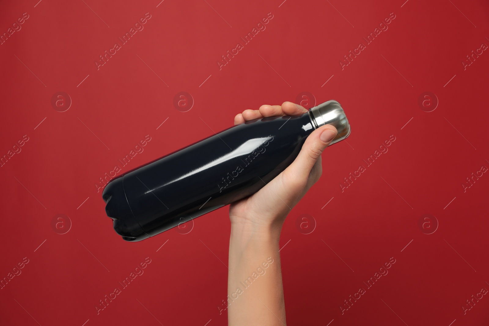 Photo of Woman holding modern dark thermos on red background, closeup