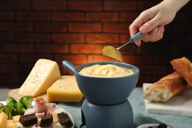 Photo of Woman dipping piece of potato into fondue pot with melted cheese at table with snacks, closeup