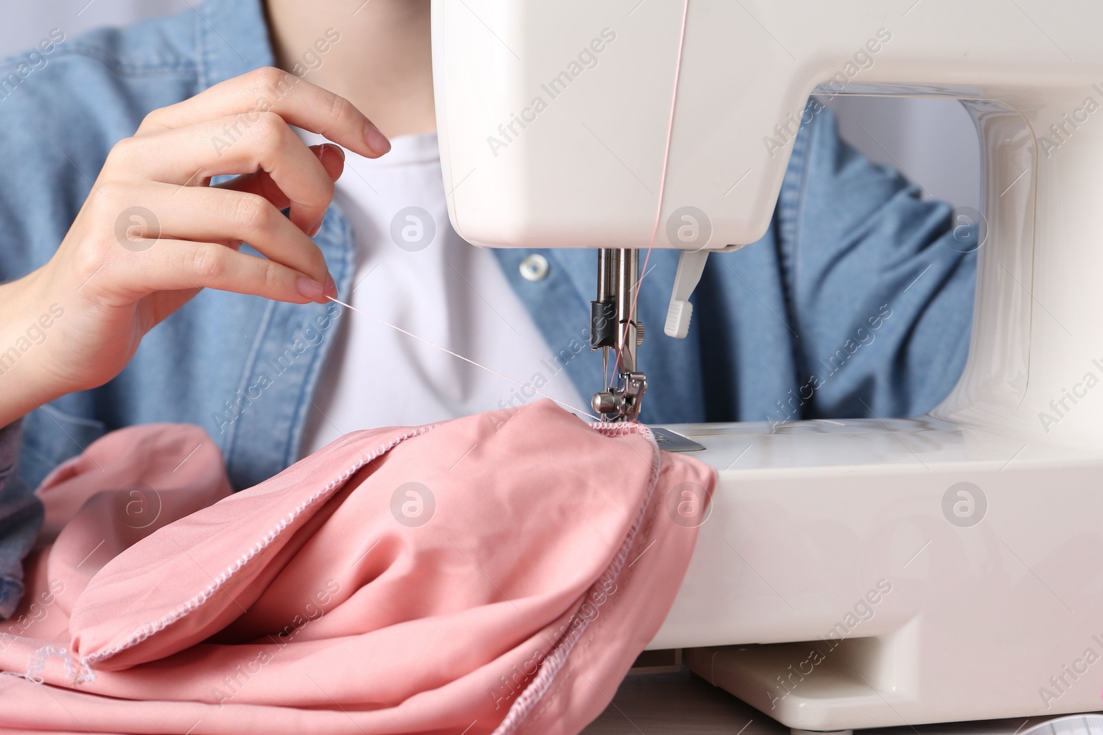 Photo of Seamstress working with sewing machine at table indoors, closeup