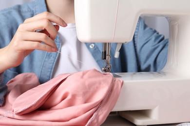 Photo of Seamstress working with sewing machine at table indoors, closeup