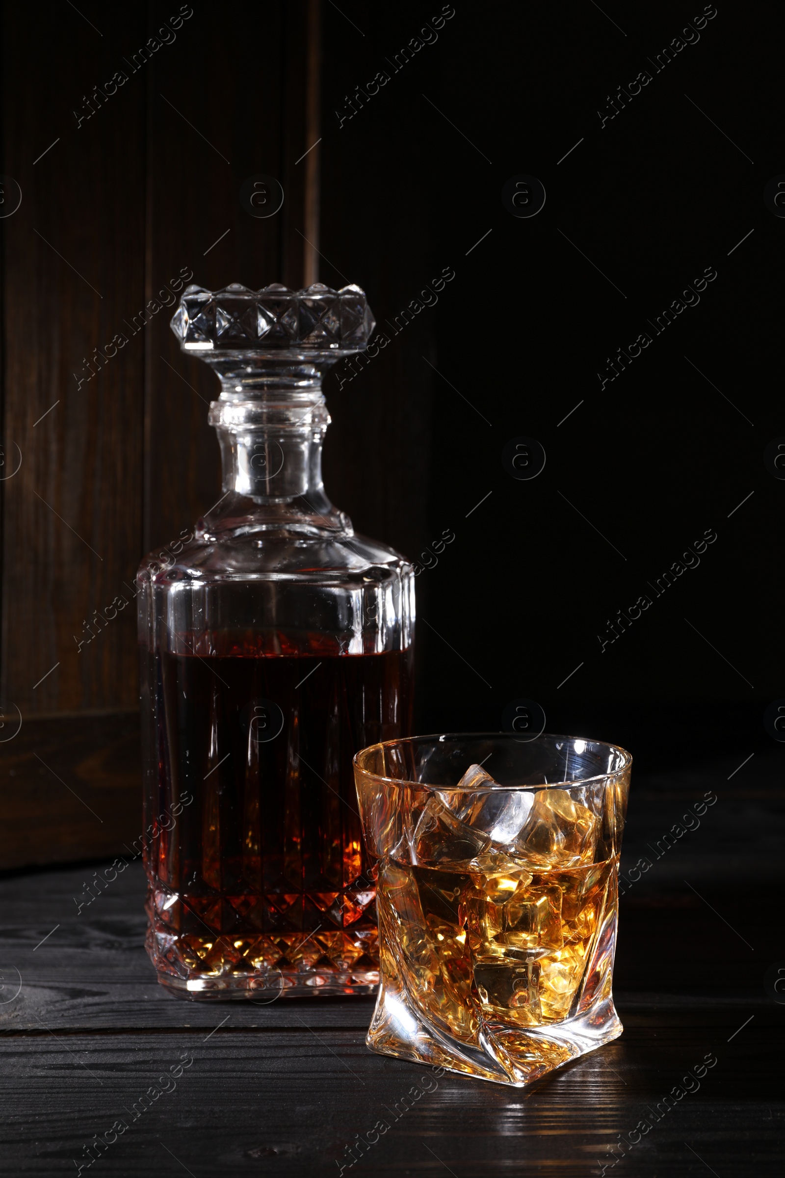 Photo of Whiskey with ice cubes in glass and bottle on black wooden table