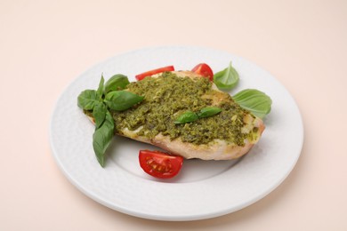 Photo of Delicious chicken breast with pesto sauce, tomatoes and basil on beige table, closeup