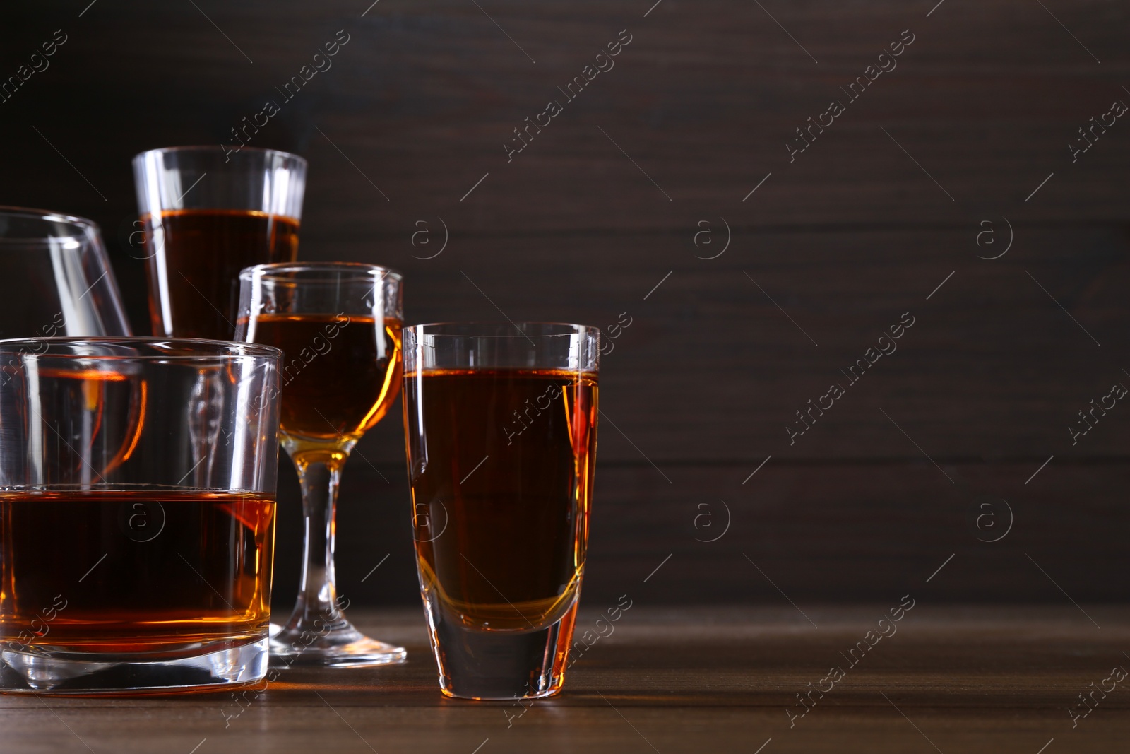 Photo of Different delicious liqueurs in glasses on wooden table, space for text