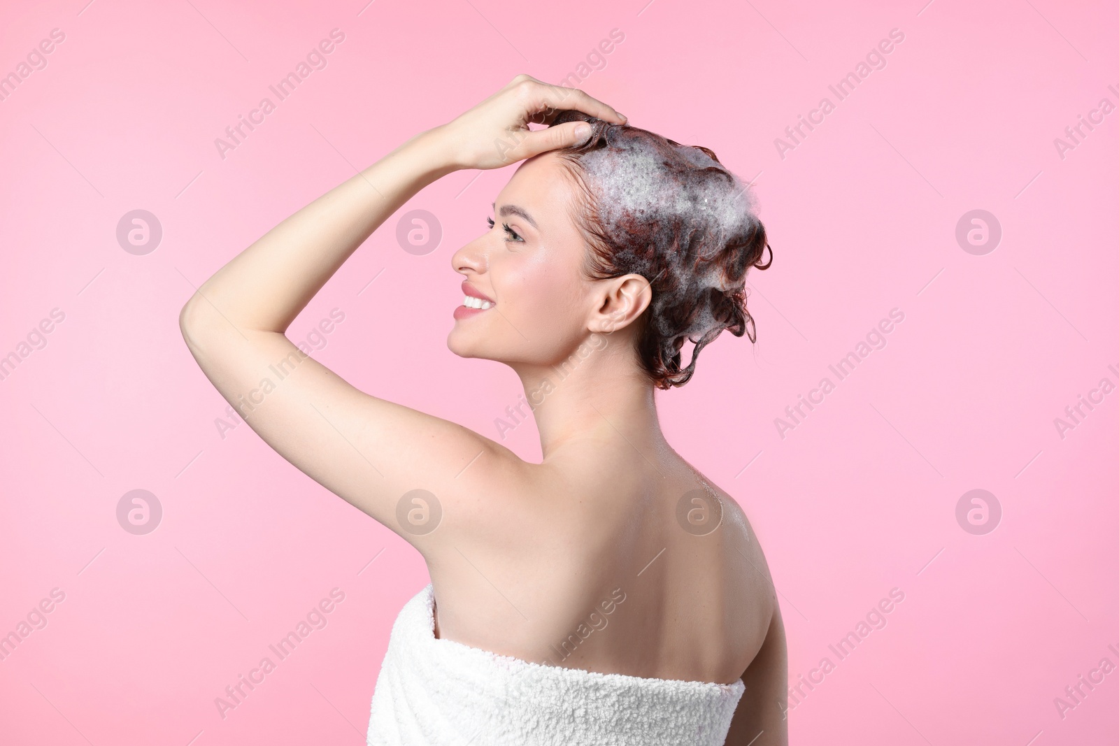 Photo of Happy young woman washing her hair with shampoo on pink background