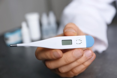 Photo of Doctor holding thermometer against blurred background, closeup. Medical objects