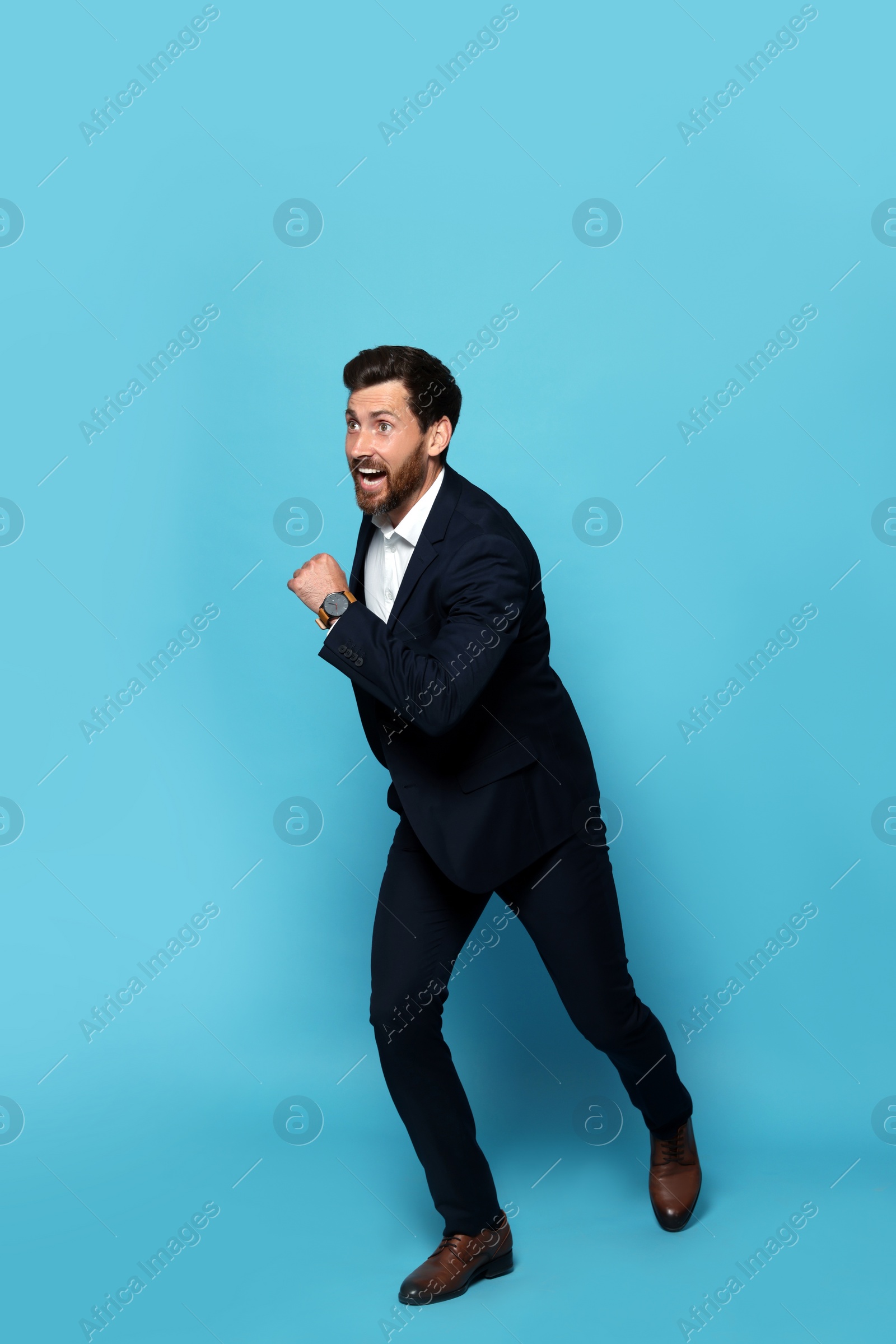 Photo of Handsome bearded man in suit running on light blue background