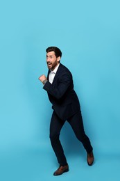 Photo of Handsome bearded man in suit running on light blue background