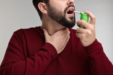 Young man using throat spray on grey background, closeup