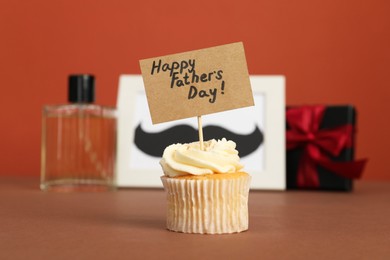 Happy Father's Day. Tasty cupcake with greetings in front of presents on brown table, closeup