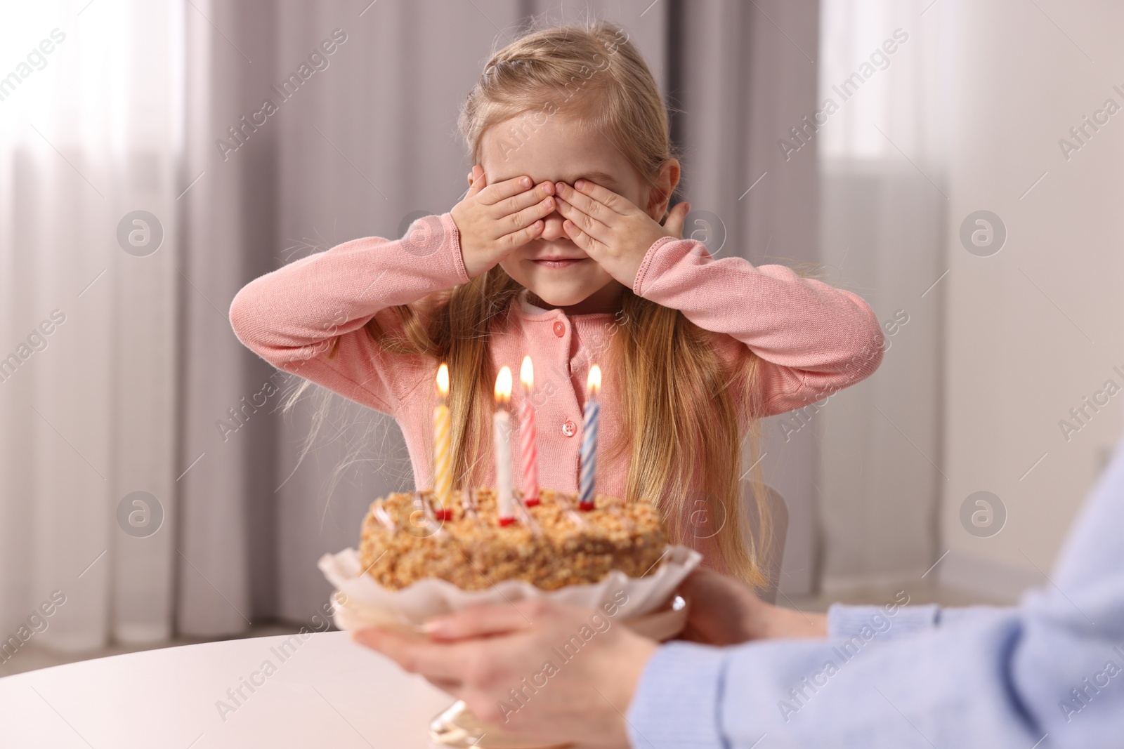 Photo of Birthday celebration. Mother holding tasty cake with burning candles near her daughter indoors