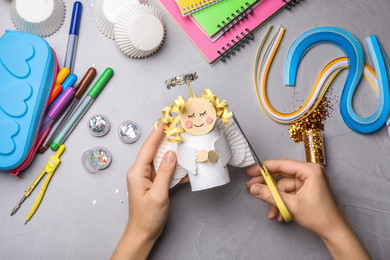 Woman making toy angel from toilet paper hub at grey table, top view