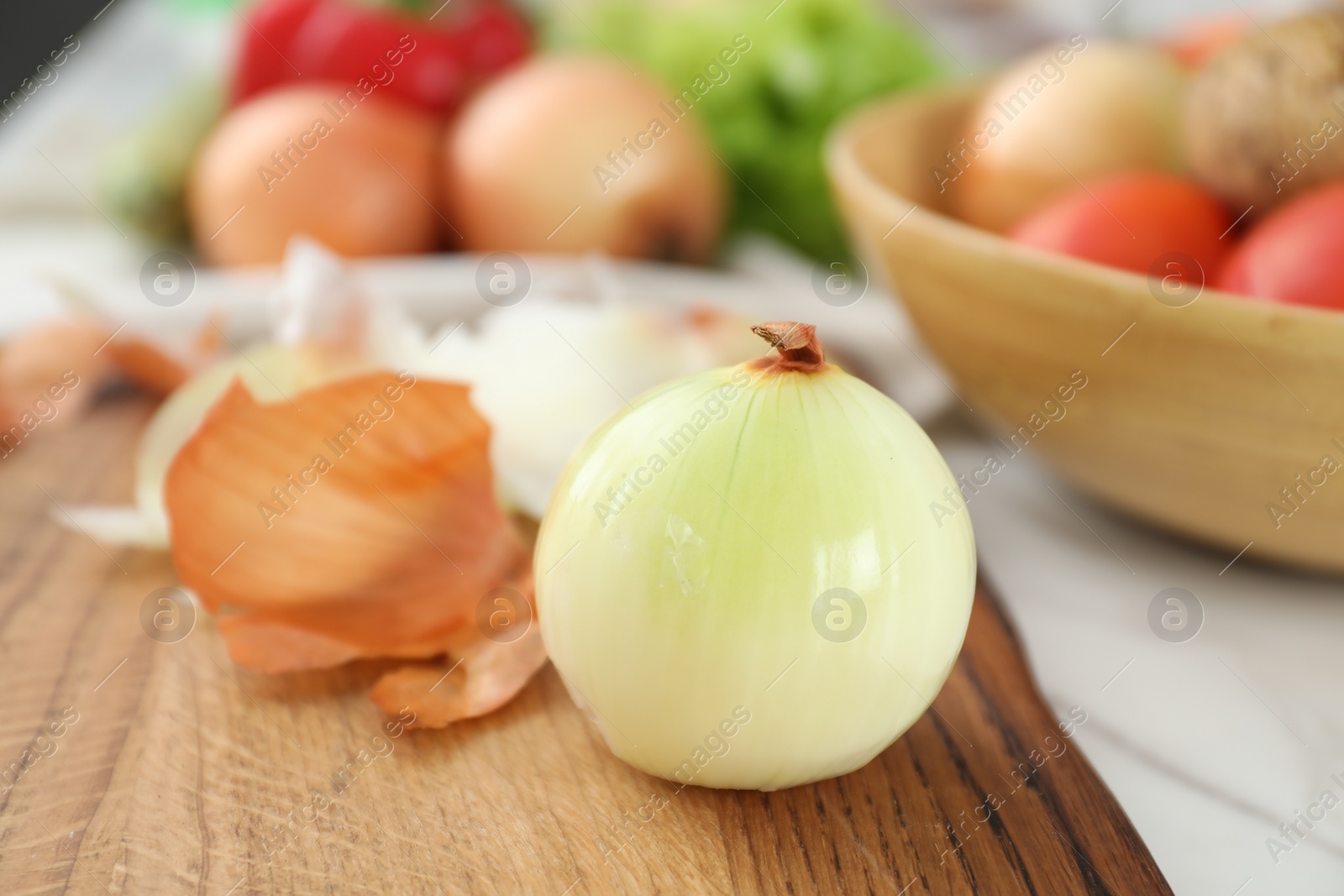 Photo of Wooden board with fresh onion and peels on table, closeup