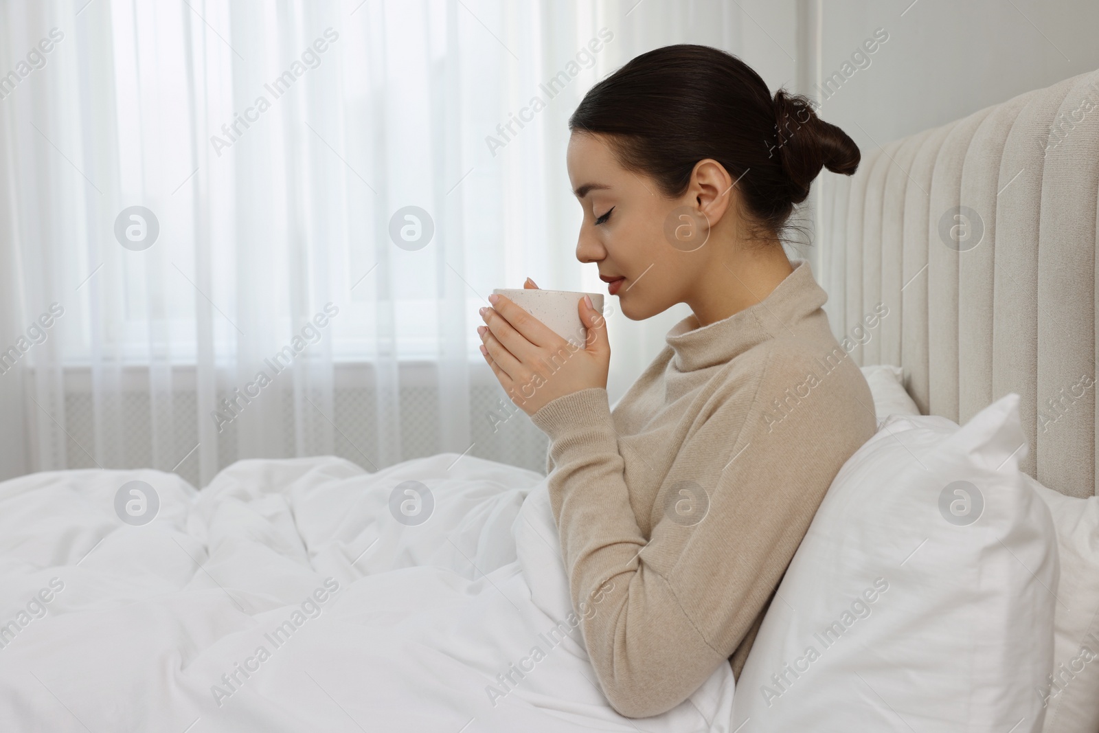 Photo of Beautiful young woman with cup of drink in bed at home