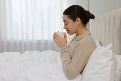 Photo of Beautiful young woman with cup of drink in bed at home