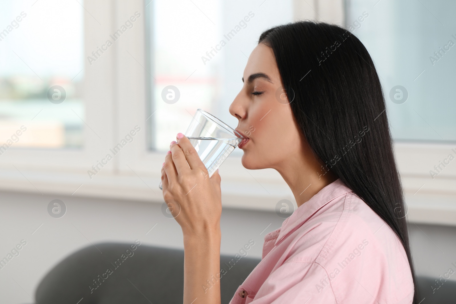Photo of Beautiful young woman drinking water indoors, space for text. Refreshing drink