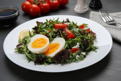 Delicious salad with boiled egg, arugula and tomatoes on black table, closeup