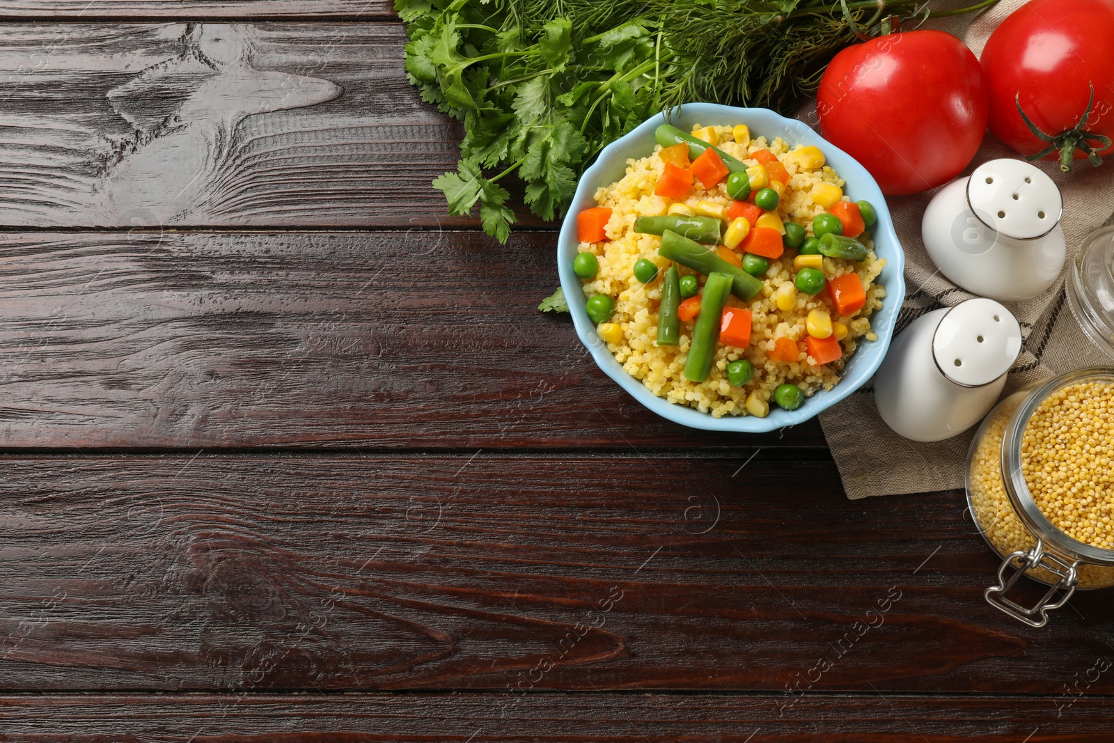 Photo of Tasty millet porridge with vegetables in bowl and products on wooden table, flat lay. Space for text