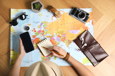 Photo of Woman with smartphone and world map planning trip at wooden table, top view