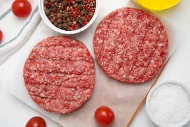 Raw hamburger patties with spices and tomatoes on white table, flat lay