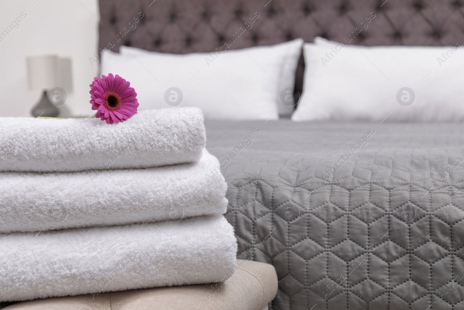 Photo of Stack of fresh towels on bedside bench in hotel room