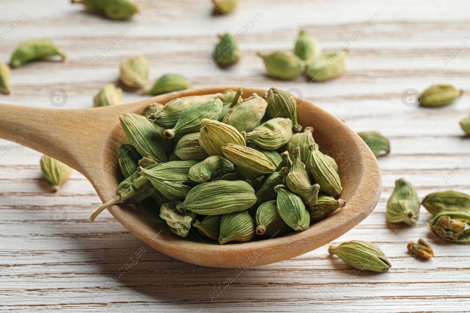 Photo of Spoon with dry cardamom pods on white wooden table, closeup