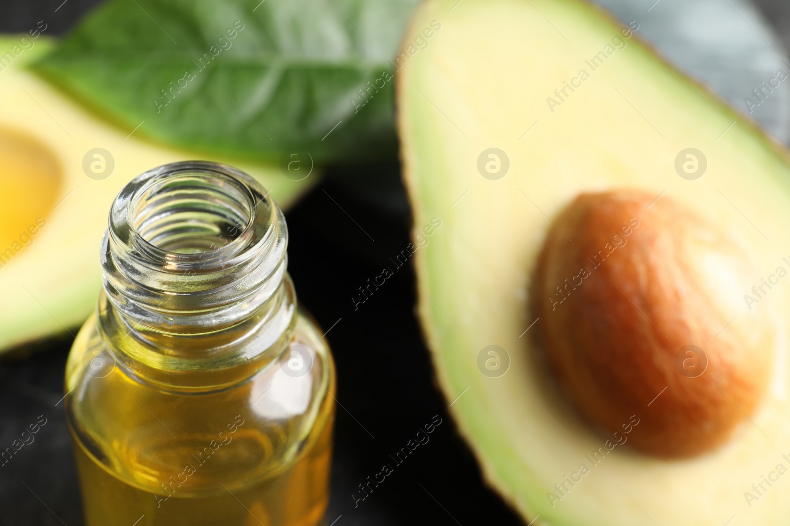 Photo of Bottle of essential oil and cut avocado on table, closeup
