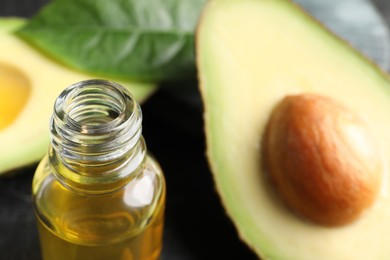Bottle of essential oil and cut avocado on table, closeup