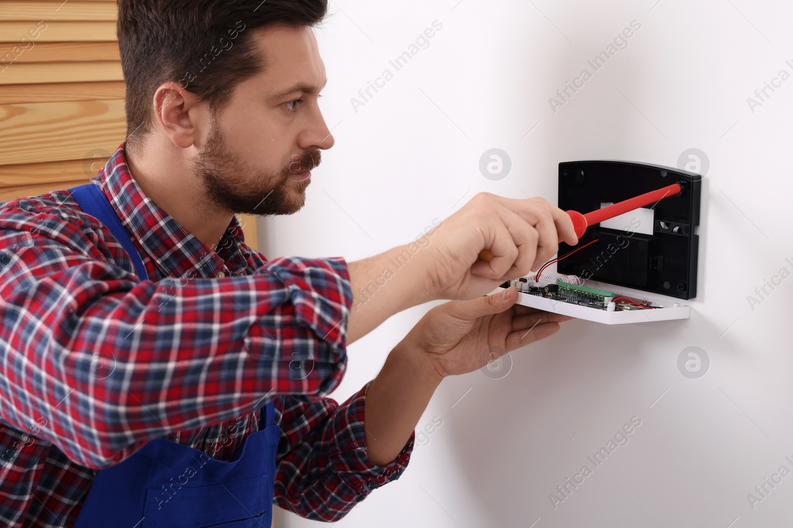 Photo of Technician installing home security alarm system on white wall indoors