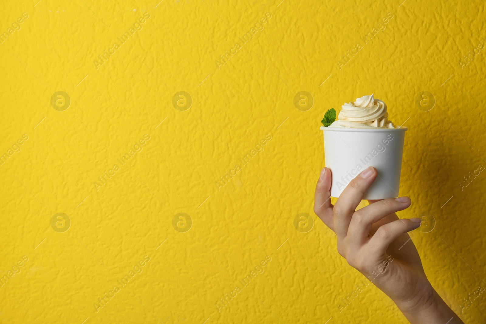 Photo of Woman holding cup with tasty frozen yogurt on yellow background, closeup. Space for text