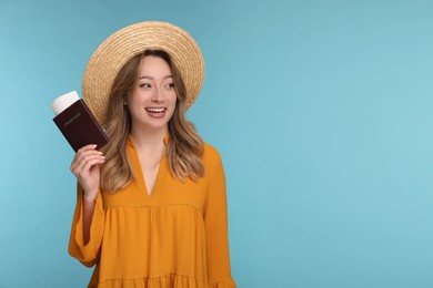 Photo of Happy young woman with passport, ticket and hat on light blue background, space for text