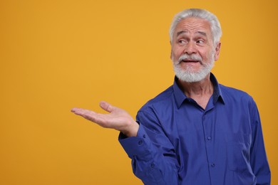 Photo of Special promotion. Senior man showing something on orange background. Space for text