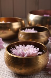 Photo of Tibetan singing bowls with water and beautiful flowers on table, closeup
