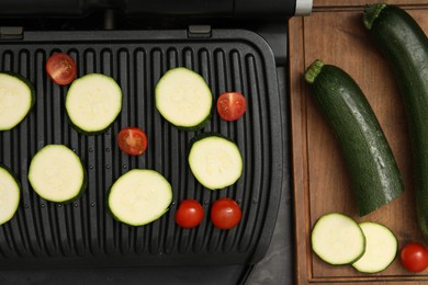 Photo of Electric grill with vegetables on black table, flat lay