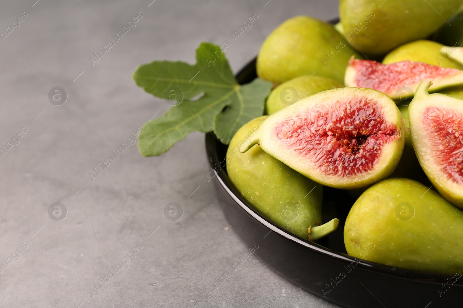 Photo of Cut and whole green figs on light gray table, closeup. Space for text
